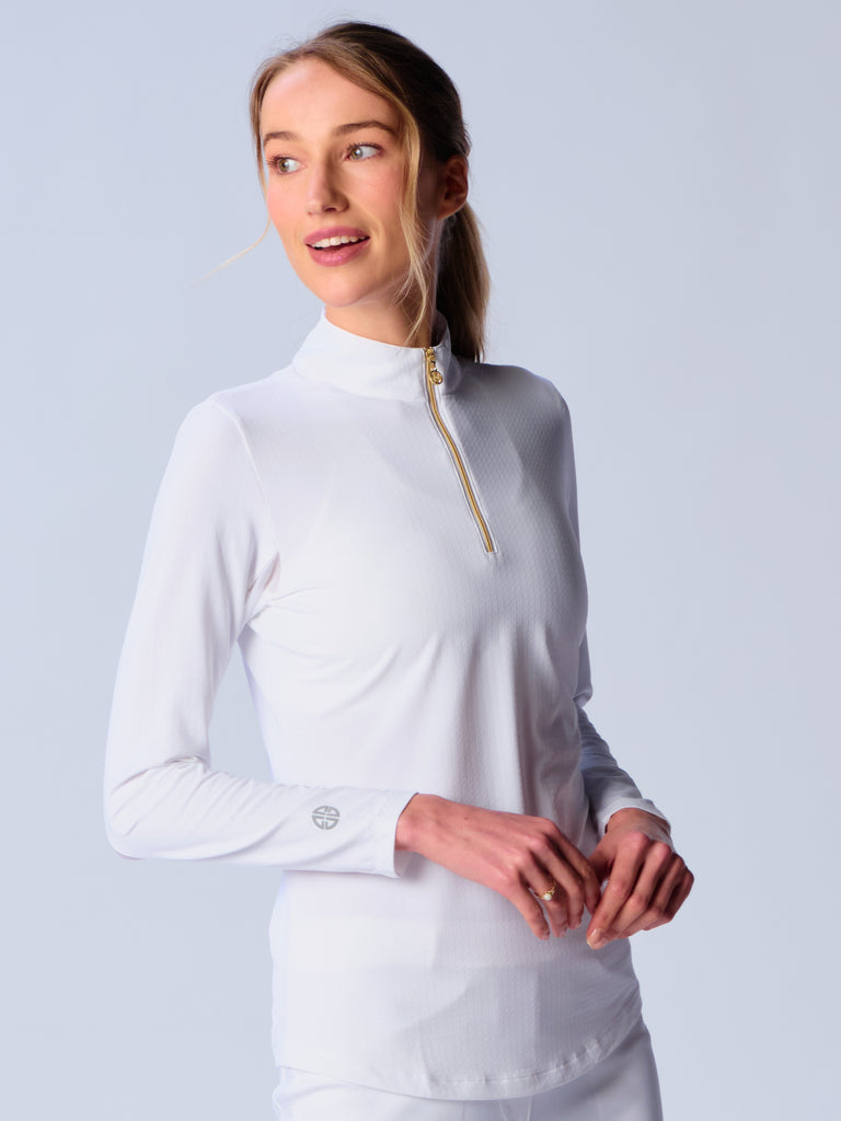 A woman wears G Lifestyle Quarter Zip Sun Protection Top in White. The top is designed with long sleeves and features an adjustable mock neck collar with a gold-toned quarter zip, the brand’s logo discreetly placed on the right wrist. The fabric appears to have a lightweight, subtle texture, that likely offers menthol cooling, moisture wicking properties, breathability, sun safety and comfort. Suitable for various outdoor athletic activities such as golf, tennis, padel tennis, pickleball or even cycling.