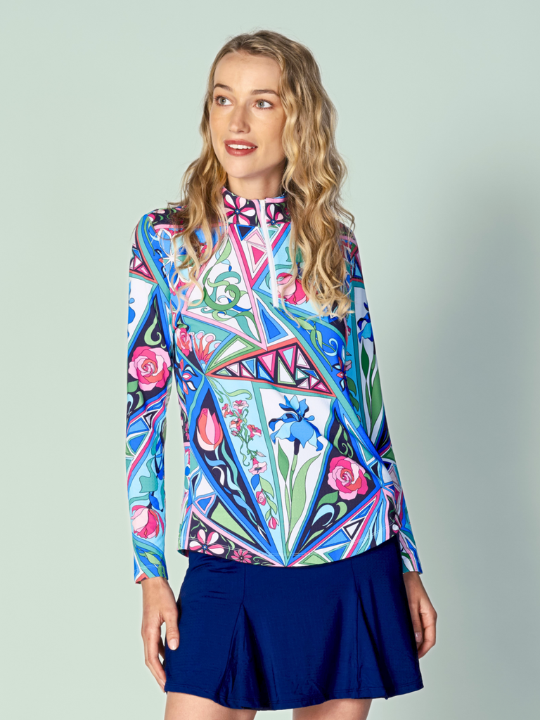 A woman models the G Lifestyle Quarter Zip Sun Protection Top in Bermuda Multi - abstract print of the Spring Summer 2024 Collection. The top has long sleeves, an adjustable mock neck collar with a flat quarter zip. The fabric appears to have a lightweight, subtle texture, that likely offers menthol cooling, moisture wicking, breathability, sun safety and comfort. Suitable for golf, tennis, padel tennis, pickleball or even cycling.