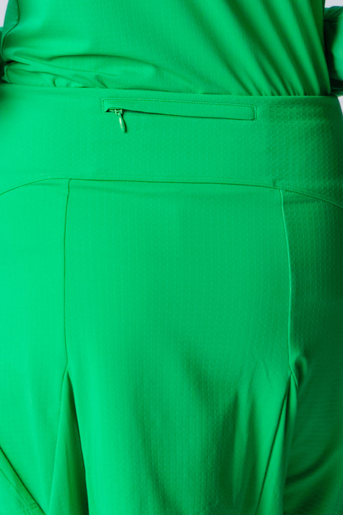 The close-up image showcases the back view of the G Lifestyle Flare Godet Skort in Kelly Green. The skort waistband is flat and wide with a single horizontal utility pocket with zip closure. The subtle texture of the soft stretchy fabric is noticeable. The stitching is meticulous, ensuring a durable and comfortable fit. This skort is suitable for tennis, pickleball, padel tennis, golf.