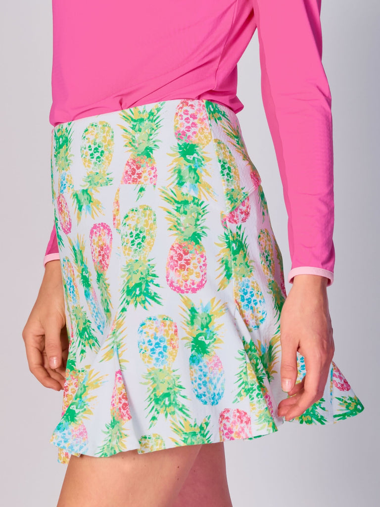 A woman pictured while twirling, showcasing the G Lifestyle Flare Godet Skort in Ananas Green - tropical print of the Spring Summer 2024 Collection. This feminine and sporty skort features a fitted waistband and a flared hem with godet inserts, giving the garment playful and flirty silhouette. The length of the skort appears to be mid-thigh. The fabric looks soft, comfortable, and stretchy. This skort is suitable for tennis, pickleball, padel tennis, golf.