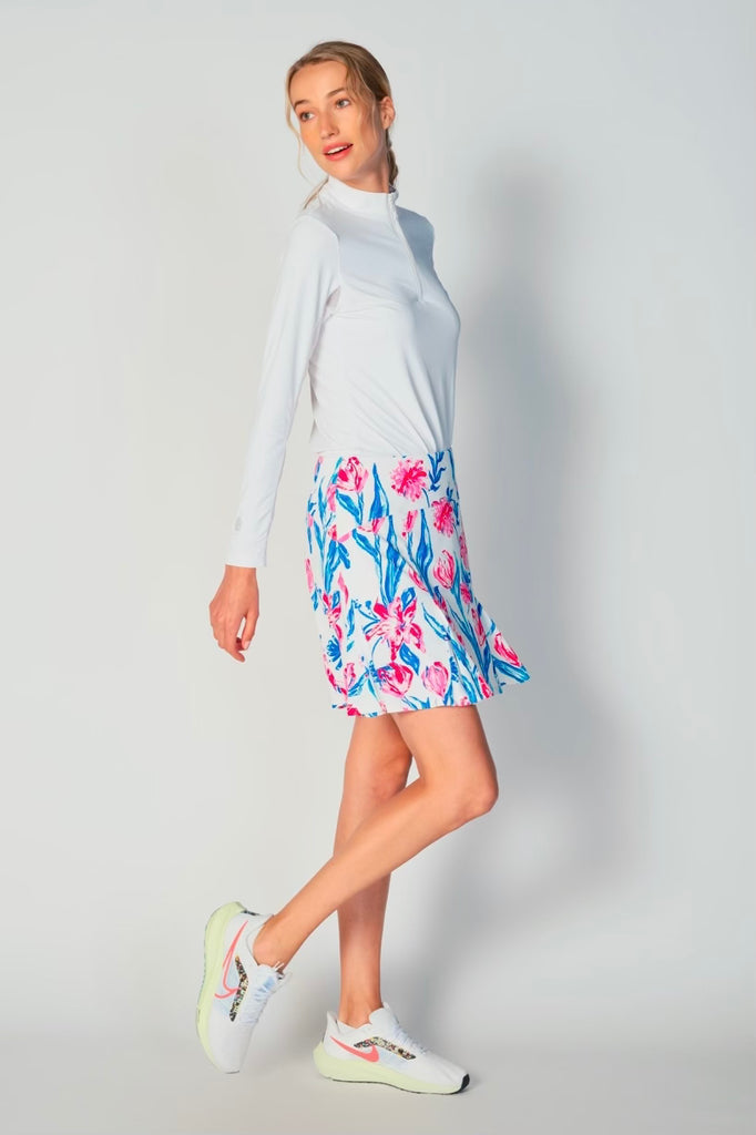 A woman pictured from the side, showcasing the G Lifestyle Flare Godet Skort in Tulip - floral print of the Spring Summer 2024 Collection. This feminine and sporty skort features a fitted waistband and a flared hem with godet inserts, giving the garment playful and flirty silhouette. The length of the skort appears to be mid-thigh. The fabric looks soft, comfortable, and stretchy. This skort is suitable for tennis, pickleball, padel tennis, golf.
