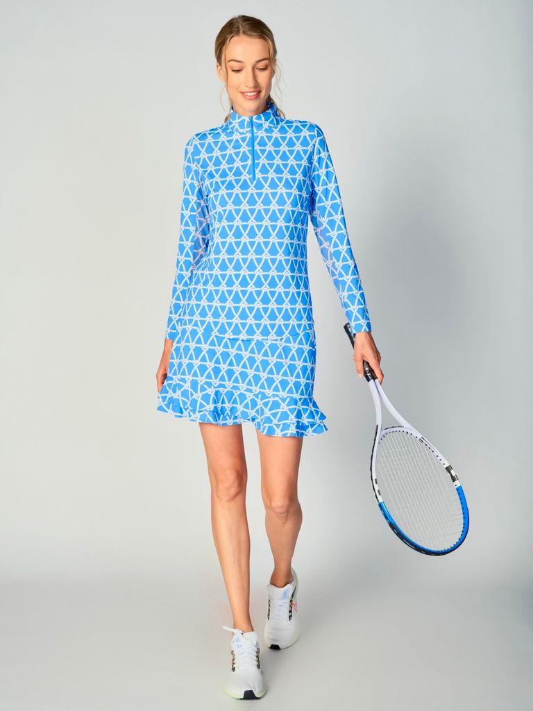 A woman is holding a tennis racket, showcasing a G Lifestyle Quarter Zip Sun Protection Top in Nautical Bright Peri – marine-inspired rope-knot print from Spring Summer 2024 Collection. The top has long sleeves, an adjustable mock neck collar with a flat quarter zip. The fabric appears to have a lightweight, subtle texture, that likely offers menthol cooling, moisture wicking, breathability, sun safety and comfort. Suitable for golf, tennis, padel tennis, pickleball or even cycling.