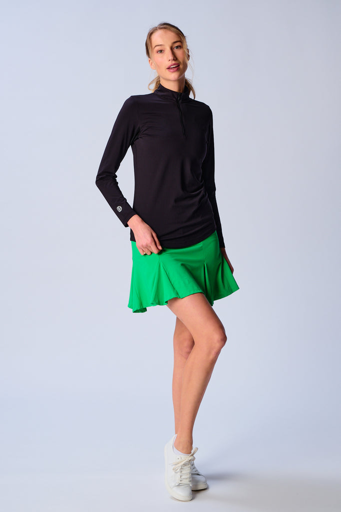 A woman wears G Lifestyle Quarter Zip Sun Protection Top in Black. The top has long sleeves, an adjustable mock neck collar with a flat quarter zip, the brand’s logo discreetly placed on the right wrist. The fabric appears to have a lightweight, subtle texture, that likely offers menthol cooling, moisture wicking, breathability, sun safety and comfort. Suitable for golf, tennis, padel tennis, pickleball or even cycling.