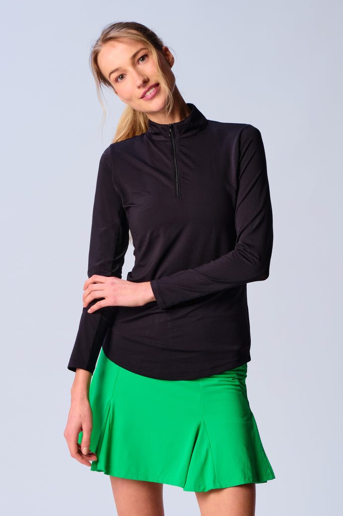 A woman wears G Lifestyle Quarter Zip Sun Protection Top in Black. The top has long sleeves, an adjustable mock neck collar with a flat quarter zip, the brand’s logo discreetly placed on the right wrist. The fabric appears to have a lightweight, subtle texture, that likely offers menthol cooling, moisture wicking, breathability, sun safety and comfort. Suitable for golf, tennis, padel tennis, pickleball or even cycling.