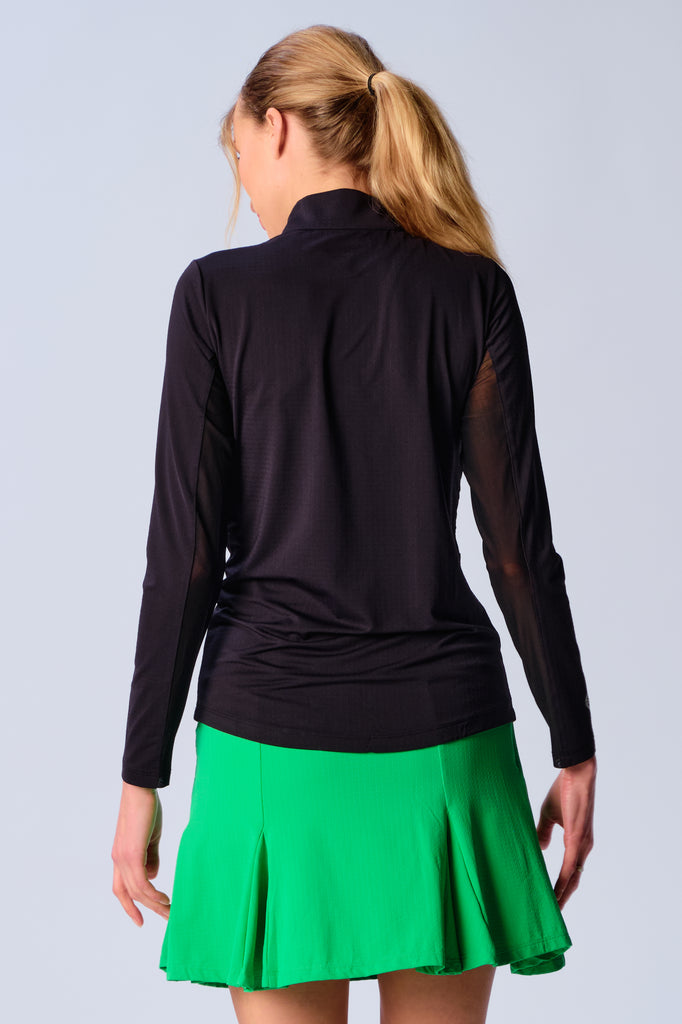 A woman is showcasing the back of the G Lifestyle Quarter Zip Sun Protection Top in Black. The top is tailored with a form-fitting silhouette, complete with long sleeves and a high collar for maximum sun protection. Notably, it includes smooth mesh underarm inserts, which are seamlessly integrated for enhanced breathability, ensuring comfort during active use. 