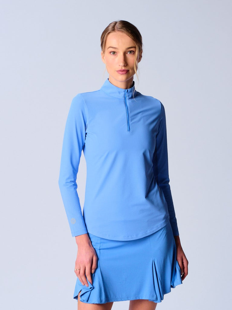 A woman wears G Lifestyle Quarter Zip Sun Protection Top in Bright Peri. The top has long sleeves, an adjustable mock neck collar with a flat quarter zip, the brand’s logo discreetly placed on the right wrist. The fabric appears to have a lightweight, subtle texture, that likely offers menthol cooling, moisture wicking, breathability, sun safety and comfort. Suitable for golf, tennis, padel tennis, pickleball or even cycling.
