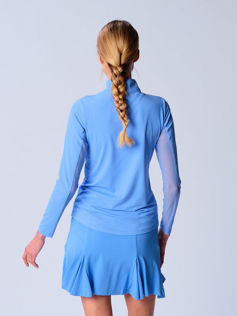 A woman is showcasing the back of the G Lifestyle Quarter Zip Sun Protection Top in Bright Peri. The top is tailored with a form-fitting silhouette, complete with long sleeves and a high collar for maximum sun protection. Notably, it includes smooth mesh underarm inserts, which are seamlessly integrated for enhanced breathability, ensuring comfort during active use.
