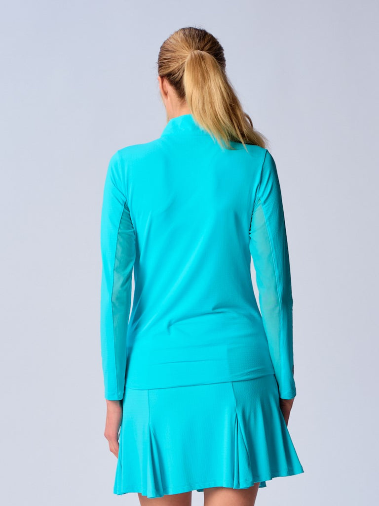 A woman is showcasing the back of the G Lifestyle Quarter Zip Sun Protection Top in Caribbean Turquoise. The top is tailored with a form-fitting silhouette, complete with long sleeves and a high collar for maximum sun protection. Notably, it includes smooth mesh underarm inserts, which are seamlessly integrated for enhanced breathability, ensuring comfort during active use. 