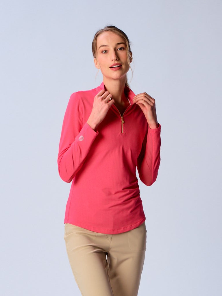A woman wears the G Lifestyle Quarter Zip Sun Protection Top in Coral. The top is designed with long sleeves and features an adjustable mock neck collar with a gold-toned quarter zip, the brand’s logo discreetly placed on the right wrist. The fabric appears to have a lightweight, subtle texture, that likely offers menthol cooling, moisture wicking properties, breathability, sun safety and comfort. Suitable for golf, tennis, padel tennis, pickleball or even cycling.