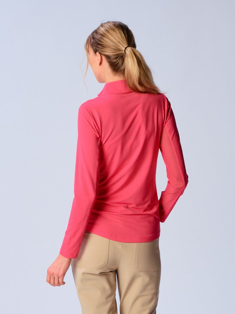 A woman is showcasing the back of the G Lifestyle Quarter Zip Sun Protection Top in Coral. The top is tailored with a form-fitting silhouette, complete with long sleeves and a high collar for maximum sun protection. Notably, it includes smooth mesh underarm inserts, which are seamlessly integrated for enhanced breathability, ensuring comfort during active use. 
