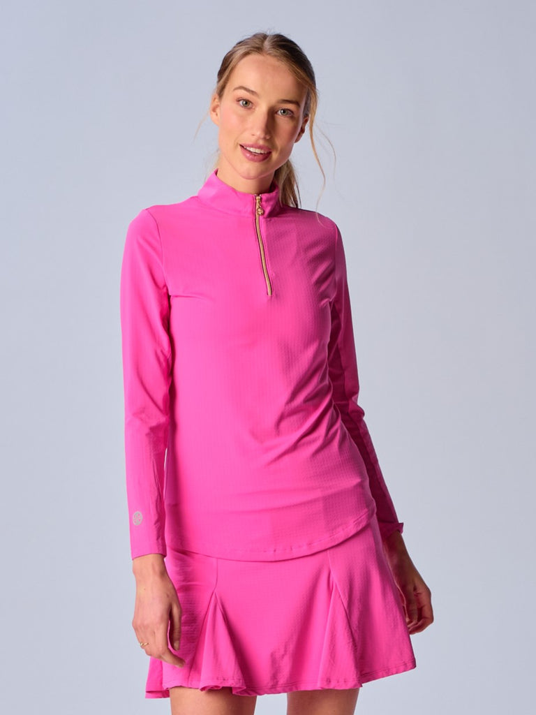 A woman wears the G Lifestyle Quarter Zip Sun Protection Top in Hot Pink. The top is designed with long sleeves and features an adjustable mock neck collar with a gold quarter zip, the brand’s logo discreetly placed on the right wrist. The fabric appears to have a lightweight, subtle texture, that likely offers menthol cooling, moisture wicking properties, breathability, sun safety and comfort. Suitable for golf, tennis, padel tennis, pickleball or even cycling.