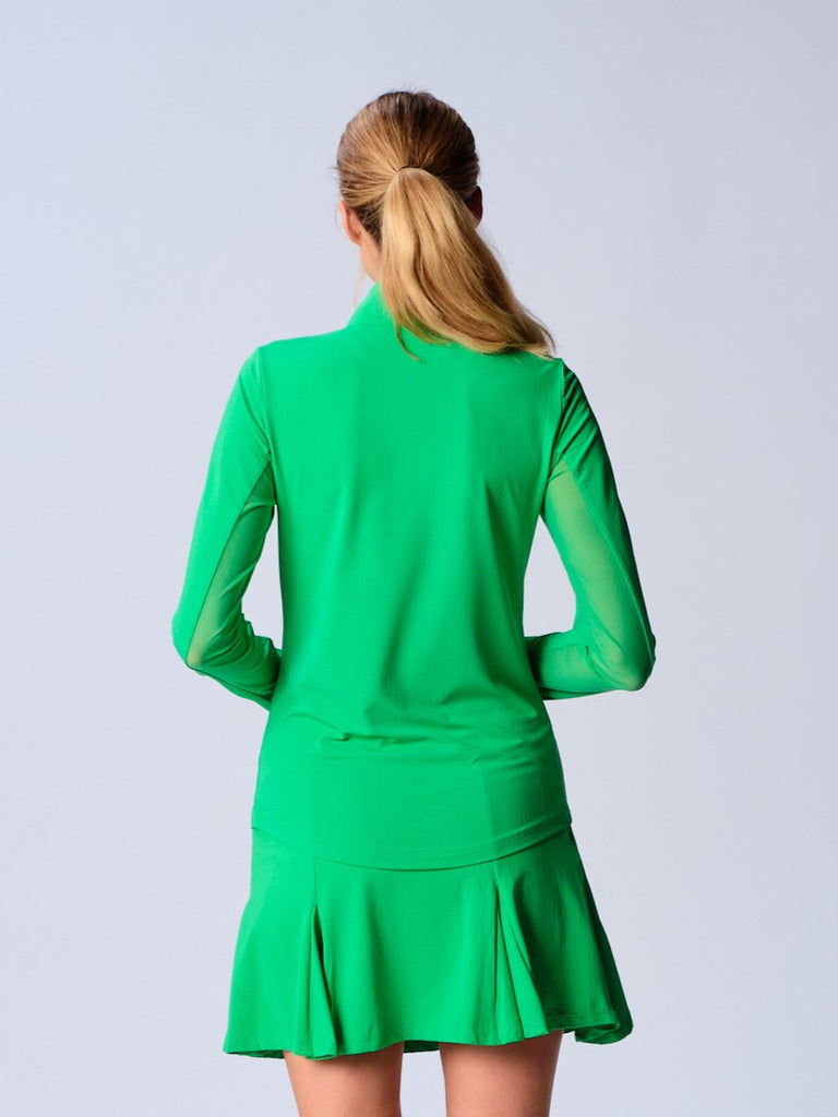 A woman is showcasing the back of the G Lifestyle Quarter Zip Sun Protection Top in Kelly Green. The top is tailored with a form-fitting silhouette, complete with long sleeves and a high collar for maximum sun protection. Notably, it includes smooth mesh underarm inserts, which are seamlessly integrated for enhanced breathability, ensuring comfort during active use.