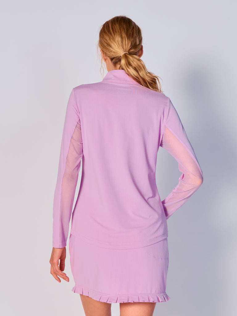 A woman is showcasing the back of the G Lifestyle Quarter Zip Sun Protection Top in Lavender. The top is tailored with a form-fitting silhouette, complete with long sleeves and a high collar for maximum sun protection. Notably, it includes smooth mesh underarm inserts, which are seamlessly integrated for enhanced breathability, ensuring comfort during active use.