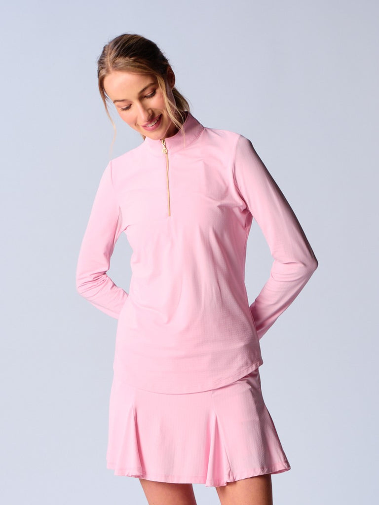 A woman wears the G Lifestyle Quarter Zip Sun Protection Top in Light Pink. The top has long sleeves and an adjustable mock neck collar with a gold quarter zip, the brand’s logo discreetly placed on the right wrist. The fabric appears to have a lightweight, subtle texture, that likely offers menthol cooling, moisture wicking properties, breathability, sun safety and comfort. Suitable for various outdoor athletic activities such as golf, tennis, padel tennis, pickleball or even cycling.