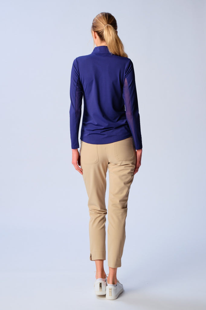 A woman is showcasing the back of the G Lifestyle Quarter Zip Sun Protection Top in Royal Blue. The top is tailored with a form-fitting silhouette, complete with long sleeves and a high collar for maximum sun protection. Notably, it includes smooth mesh underarm inserts, which are seamlessly integrated for enhanced breathability, ensuring comfort during active use. 