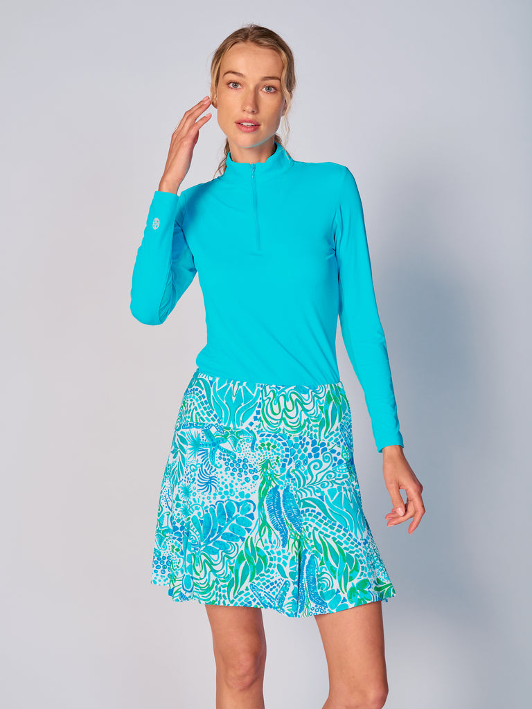 A woman stands confidently, facing camera, wears the G Lifestyle Flare Godet Skort in Starfish Bright Peri – sea-theme print of the Spring Summer 2024 Collection. The skort flares out with playful, fluted edges, emphasizing movement and feminine silhouette. The skort appears to be a med-rise and the length hits her at mid-thigh. This skort is suitable for tennis, pickleball, padel tennis, golf.