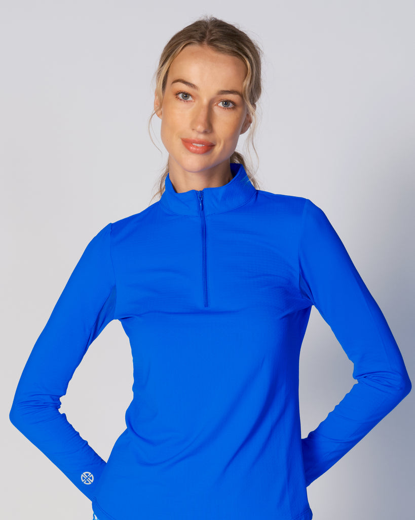 A woman wears G Lifestyle Quarter Zip Sun Protection Top in Royal Blue. The top has long sleeves, an adjustable mock neck collar with a flat quarter zip, the brand’s logo discreetly placed on the right wrist. The fabric appears to have a lightweight, subtle texture, that likely offers menthol cooling, moisture wicking, breathability, sun safety and comfort. Suitable for golf, tennis, padel tennis, pickleball or even cycling.