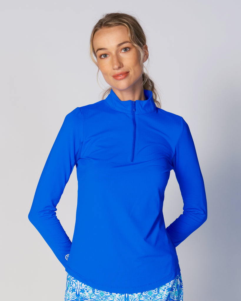 A woman wears G Lifestyle Quarter Zip Sun Protection Top in Royal Blue. The top has long sleeves, an adjustable mock neck collar with a flat quarter zip, the brand’s logo discreetly placed on the right wrist. The fabric appears to have a lightweight, subtle texture, that likely offers menthol cooling, moisture wicking, breathability, sun safety and comfort. Suitable for golf, tennis, padel tennis, pickleball or even cycling.