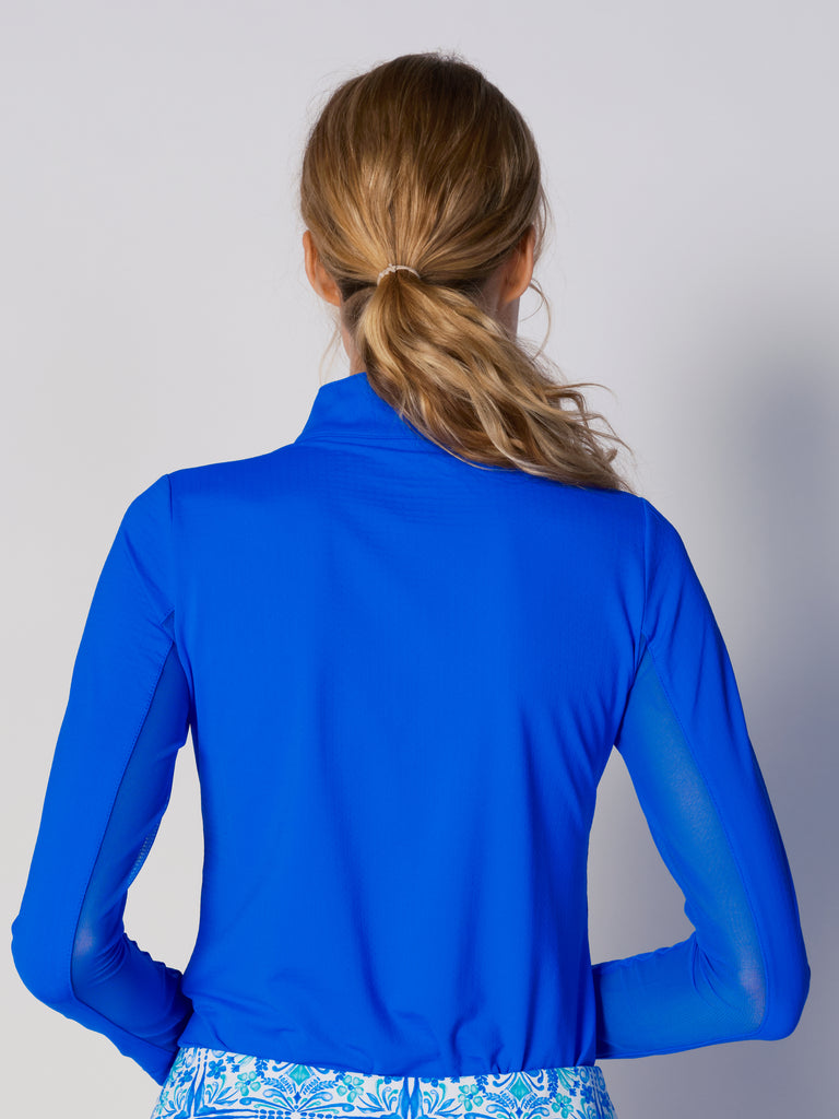 A woman is showcasing the back of the G Lifestyle Quarter Zip Sun Protection Top in Royal Blue. The top is tailored with a form-fitting silhouette, complete with long sleeves and a high collar for maximum sun protection. Notably, it includes smooth mesh underarm inserts, which are seamlessly integrated for enhanced breathability, ensuring comfort during active use. 