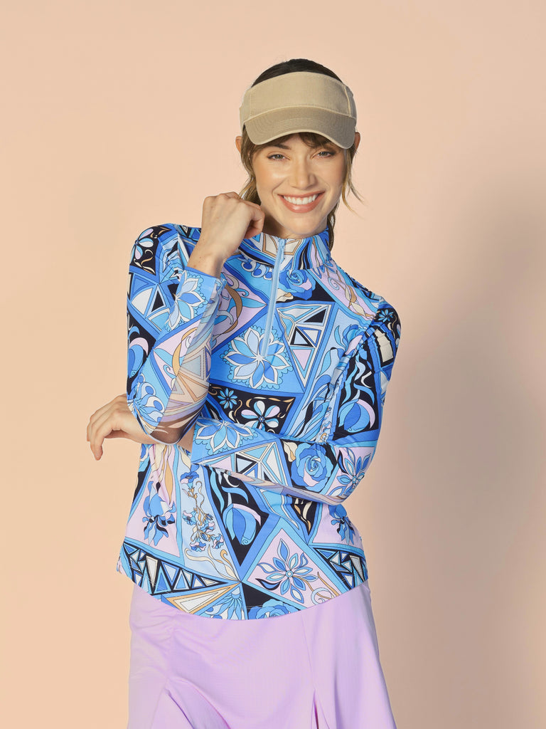 A woman models the G Lifestyle Quarter Zip Sun Protection Top in Bermuda Blue - abstract print of the Spring Summer 2024 Collection. The top has long sleeves, an adjustable mock neck collar with a flat quarter zip. The fabric appears to have a lightweight, subtle texture, that likely offers menthol cooling, moisture wicking, breathability, sun safety and comfort. Suitable for golf, tennis, padel tennis, pickleball or even cycling.