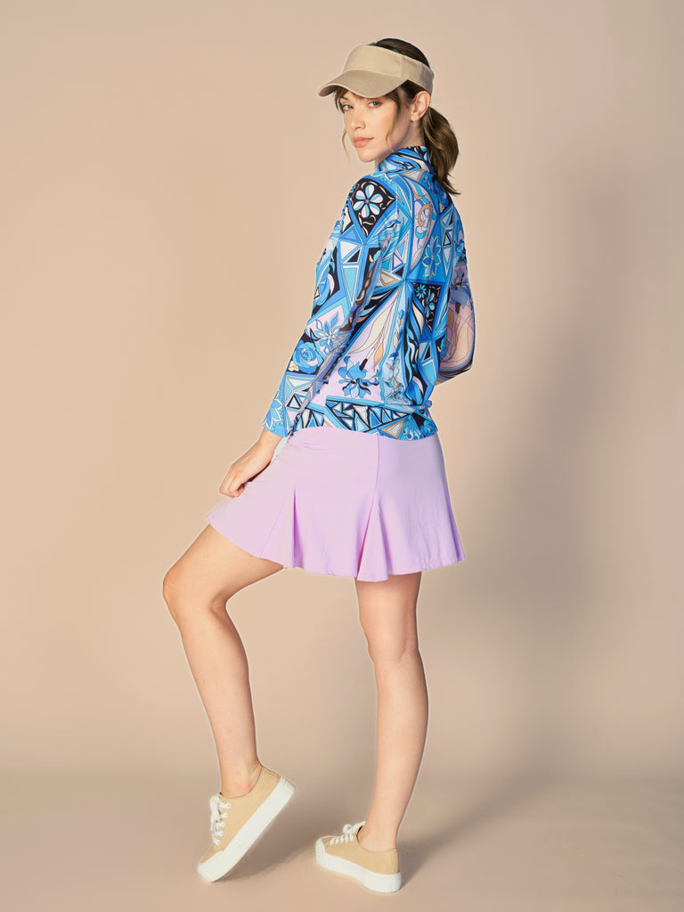 A woman is showcasing the back of the G Lifestyle Quarter Zip Sun Protection Top in Bermuda Blue -abstract print of the Spring Summer 2024 Collection. The top is tailored with a form-fitting silhouette, complete with long sleeves and a high collar for maximum sun protection. Notably, it includes smooth mesh underarm inserts, which are seamlessly integrated for enhanced breathability, ensuring comfort during active use. 