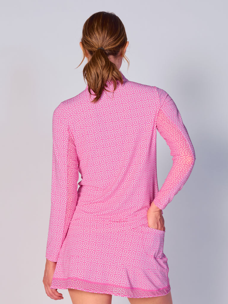A woman is showcasing the back of the G Lifestyle Quarter Zip Sun Protection Top Cubic Hot Pink - geometric print of the Spring Summer 2024 Collection. The top is tailored with a form-fitting silhouette, complete with long sleeves and a high collar for maximum sun protection. Notably, it includes smooth mesh underarm inserts, which are seamlessly integrated for enhanced breathability, ensuring comfort during active use.