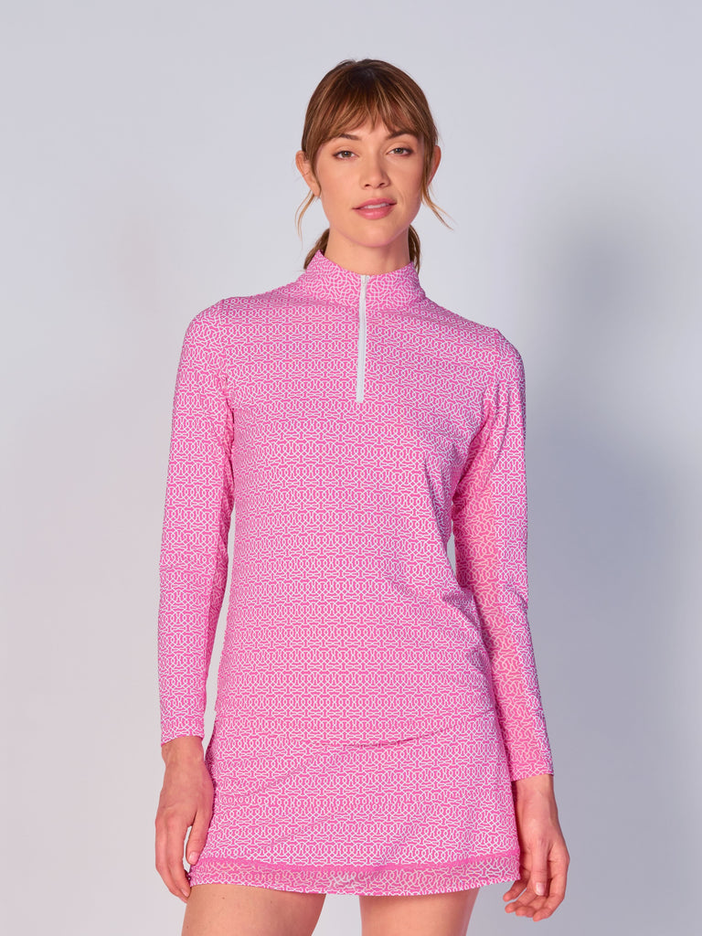 A woman wears the G Lifestyle Quarter Zip Sun Protection Top in Cubic Hot Pink - geometric print of the Spring Summer 2024 Collection. The top has long sleeves, an adjustable mock neck collar with a flat quarter zip. The fabric appears to have a lightweight, subtle texture, that likely offers menthol cooling, moisture wicking, breathability, sun safety and comfort. Suitable for golf, tennis, padel tennis, pickleball or even cycling.