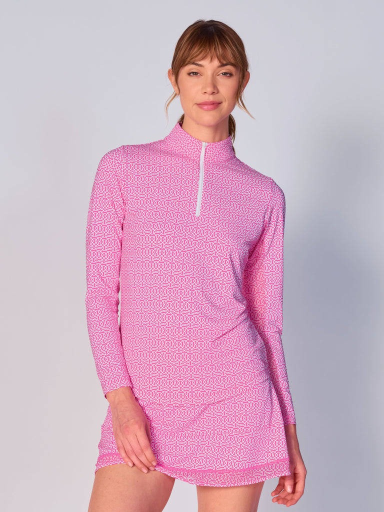 A woman wears the G Lifestyle Quarter Zip Sun Protection Top in Cubic Hot Pink - geometric print of the Spring Summer 2024 Collection. The top has long sleeves, an adjustable mock neck collar with a flat quarter zip. The fabric appears to have a lightweight, subtle texture, that likely offers menthol cooling, moisture wicking, breathability, sun safety and comfort. Suitable for golf, tennis, padel tennis, pickleball or even cycling.