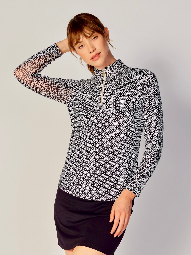 A woman wears the G Lifestyle Quarter Zip Sun Protection Top in Cubic Black - geometric print of the Spring Summer 2024 Collection. The top has long sleeves, an adjustable mock neck collar with a gold quarter zip, logo placed on the right wrist. The fabric appears to have a lightweight, subtle texture, that likely offers menthol cooling, moisture wicking, breathability, sun safety and comfort. Suitable for various outdoor athletic activities such as golf, tennis, padel tennis, pickleball or even cycling.