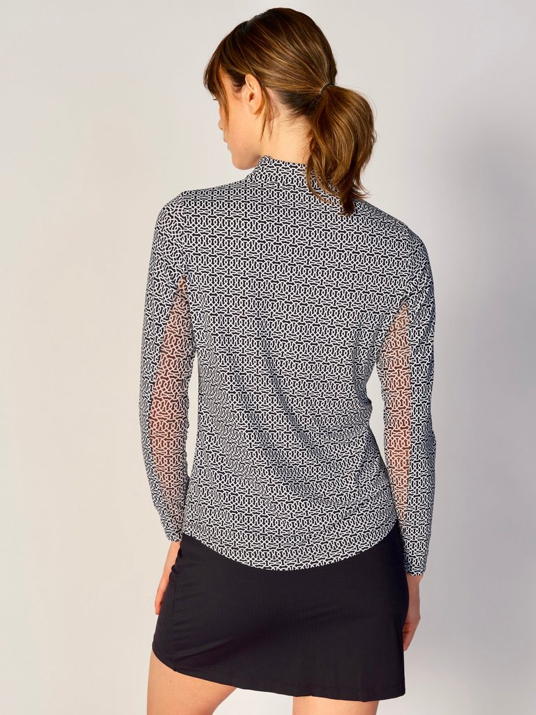 A woman is showcasing the back of the G Lifestyle Quarter Zip Sun Protection Top Cubic Black - geometric print of the Spring Summer 2024 Collection. The top is tailored with a form-fitting silhouette, complete with long sleeves and a high collar for maximum sun protection. Notably, it includes smooth mesh underarm inserts, which are seamlessly integrated for enhanced breathability, ensuring comfort during active use. 