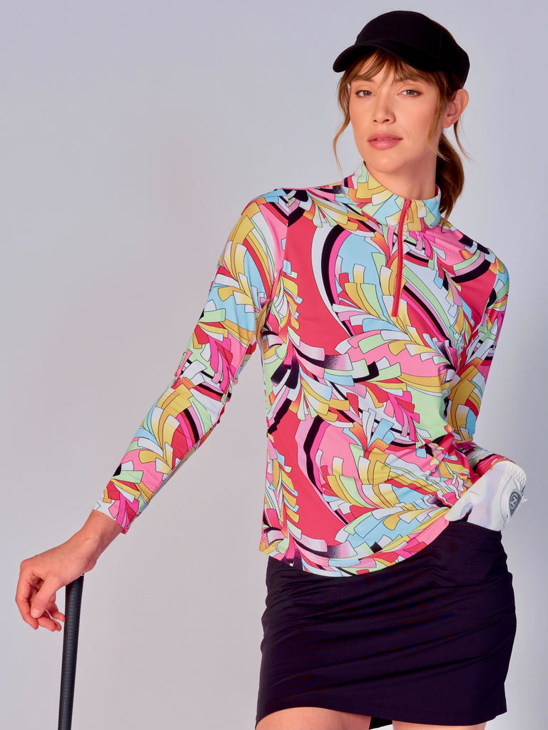 A woman is holding a golf club, showcasing a G Lifestyle Quarter Zip Sun Protection Top in St Barths Coral - abstract print of the Spring Summer 2024 Collection. The top has long sleeves, an adjustable mock neck collar with a flat quarter zip. The fabric appears to have a lightweight, subtle texture, that likely offers menthol cooling, moisture wicking, breathability, sun safety and comfort. Suitable for golf, tennis, padel tennis, pickleball or even cycling.