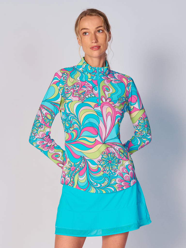 A woman models the G Lifestyle Quarter Zip Sun Protection Top in Illusion - abstract print of the Spring Summer 2024 Collection. The top has long sleeves, an adjustable mock neck collar with a flat quarter zip. The fabric appears to have a lightweight, subtle texture, that likely offers menthol cooling, moisture wicking, breathability, sun safety and comfort. Suitable for golf, tennis, padel tennis, pickleball or even cycling.