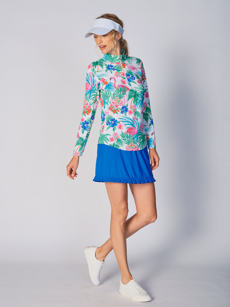 A woman models the G Lifestyle Quarter Zip Sun Protection Top in Flamingo - tropical print of the Spring Summer 2024 Collection. The top has long sleeves, an adjustable mock neck collar with a gold quarter zip, logo placed on the right wrist. The fabric appears to have a lightweight, subtle texture, that likely offers menthol cooling, moisture wicking, breathability, sun safety and comfort. Suitable for golf, tennis, padel tennis, pickleball or even cycling.