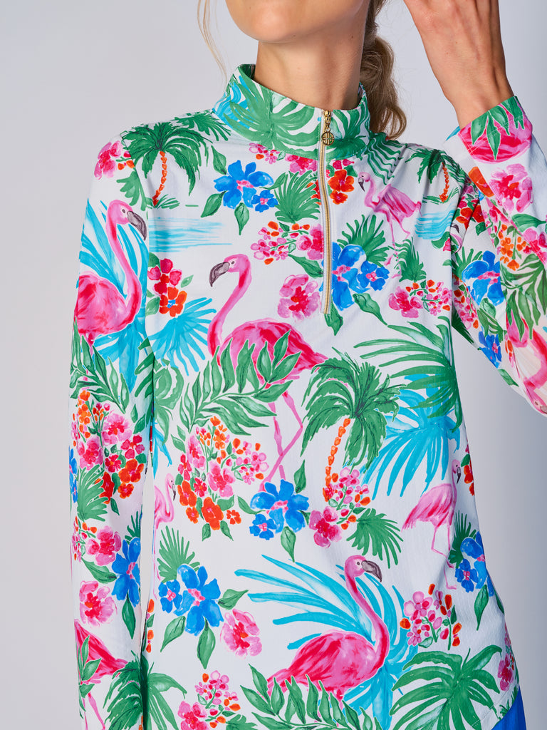 A close-up of a woman showcasing the collar of her G Lifestyle Quarter Zip Sun Protection Top in Flamingo - tropical print of the Spring Summer 2024 Collection. The top is characterized by its high neckline and a prominent quarter-zip with a circular zipper pull bearing the brand’s logo. The zipper is gold-toned, adding a touch of luxury to the top. The fabric has a texture, suggesting stretch and comfort, designed to offer sun protection. 
