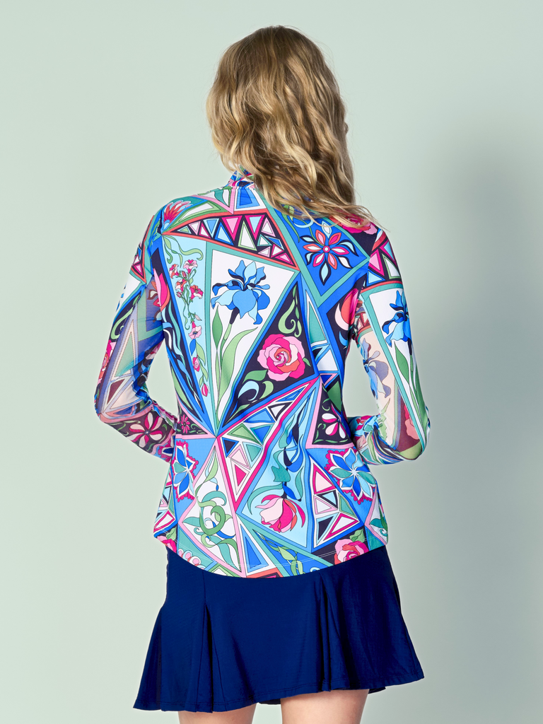 A woman is showcasing the back of the G Lifestyle Quarter Zip Sun Protection Top in Bermuda Multi -abstract print of the Spring Summer 2024 Collection. The top is tailored with a form-fitting silhouette, complete with long sleeves and a high collar for maximum sun protection. Notably, it includes smooth mesh underarm inserts, which are seamlessly integrated for enhanced breathability, ensuring comfort during active use. 