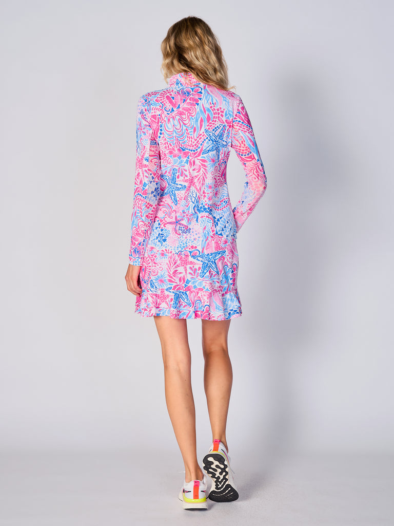 A woman is showcasing the back of the G Lifestyle Quarter Zip Sun Protection Top in Starfish Pink – sea-theme print of the Spring Summer 2024 Collection. The top is tailored with a form-fitting silhouette, complete with long sleeves and a high collar for maximum sun protection. Notably, it includes smooth mesh underarm inserts, which are seamlessly integrated for enhanced breathability, ensuring comfort during active use. 