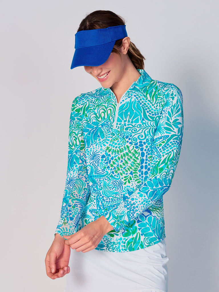 A woman models the G Lifestyle Quarter Zip Sun Protection Top in Starfish Bright Peri – sea-theme print of the Spring Summer 2024 Collection. The top has long sleeves, an adjustable mock neck collar with a flat quarter zip. The fabric appears to have a lightweight, subtle texture, that likely offers menthol cooling, moisture wicking, breathability, sun safety and comfort. Suitable for golf, tennis, padel tennis, pickleball or even cycling.