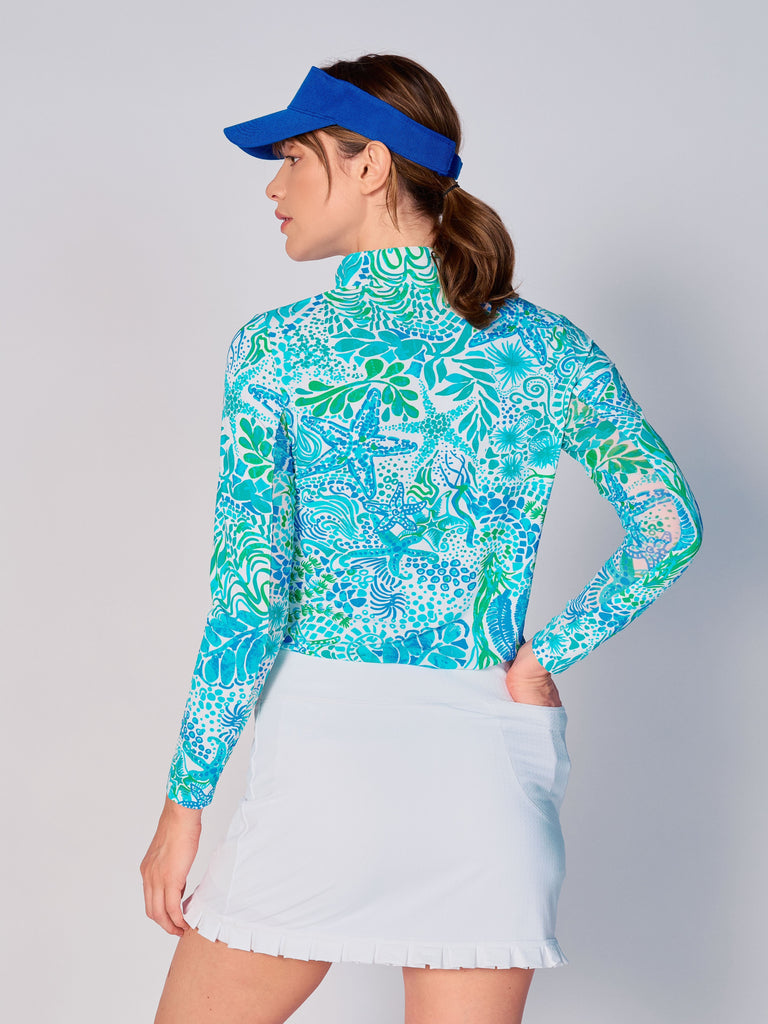 A woman is showcasing the back of the G Lifestyle Quarter Zip Sun Protection Top in Starfish Bright Peri – sea-theme print of the Spring Summer 2024 Collection. The top is tailored with a form-fitting silhouette, complete with long sleeves and a high collar for maximum sun protection. Notably, it includes smooth mesh underarm inserts, which are seamlessly integrated for enhanced breathability, ensuring comfort during active use. 