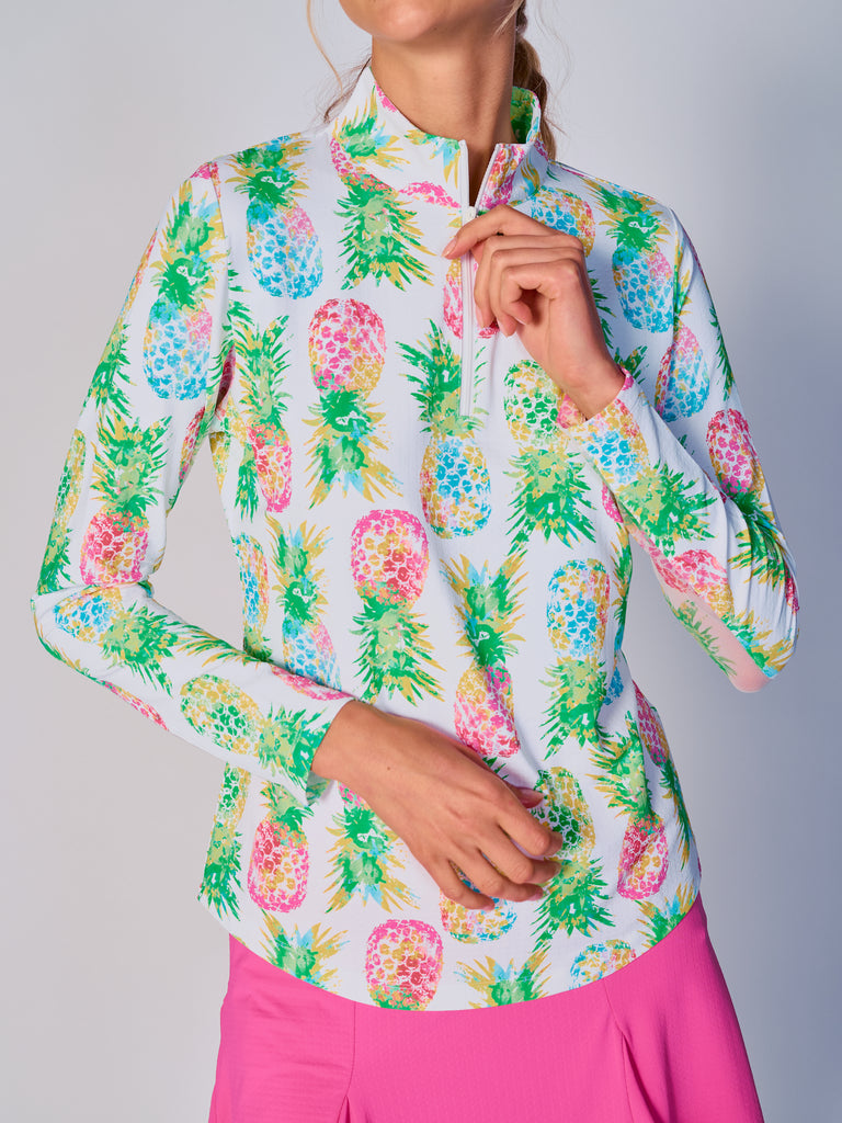 A close-up of a woman adjusting the collar of her G Lifestyle Quarter Zip Sun Protection Top in Ananas Green - tropical print of the Spring Summer 2024 Collection. The top is characterized by its high neckline and a flat quarter-zip. The fabric has a texture, suggesting stretch and comfort, designed to offer sun protection. 