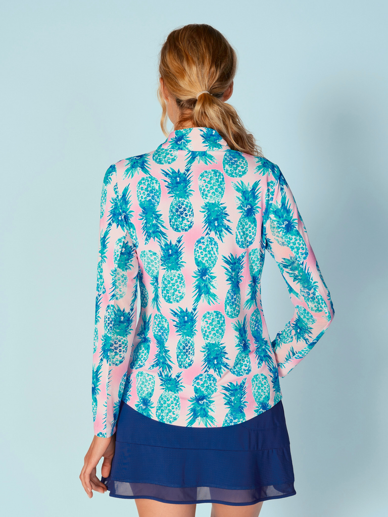 A woman is showcasing the back of the G Lifestyle Quarter Zip Sun Protection Top in Ananas Aqua - tropical print of the Spring Summer 2024 Collection. The top is tailored with a form-fitting silhouette, complete with long sleeves and a high collar for maximum sun protection. Notably, it includes smooth mesh underarm inserts, which are seamlessly integrated for enhanced breathability, ensuring comfort during active use. 