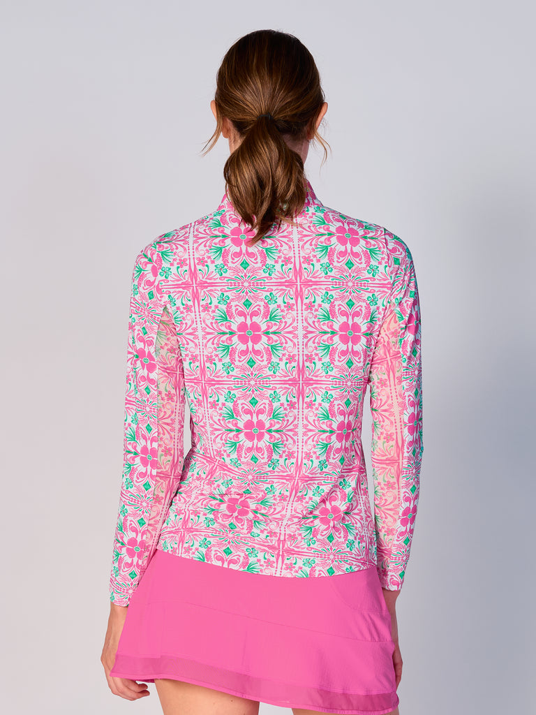 A woman is showcasing the back of the G Lifestyle Quarter Zip Sun Protection Top in Pink Tile – symmetrical ornamental print of the Spring Summer 2024 Collection. The top is tailored with a form-fitting silhouette, complete with long sleeves and a high collar for maximum sun protection. Notably, it includes smooth mesh underarm inserts, which are seamlessly integrated for enhanced breathability, ensuring comfort during active use. 