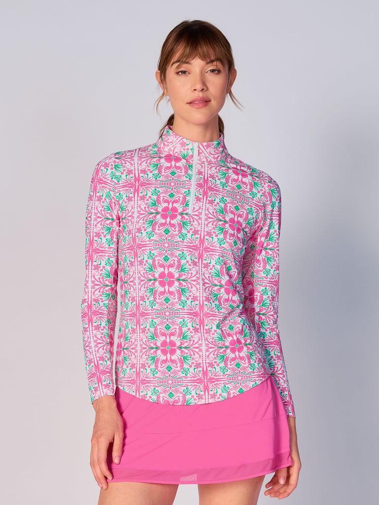 A woman models the G Lifestyle Quarter Zip Sun Protection Top in Pink Tile – symmetrical ornamental print of the Spring Summer 2024 Collection. The top has long sleeves, an adjustable mock neck collar with a flat quarter zip. The fabric appears to have a lightweight, subtle texture, that likely offers menthol cooling, moisture wicking, breathability, sun safety and comfort. Suitable for golf, tennis, padel tennis, pickleball or even cycling.