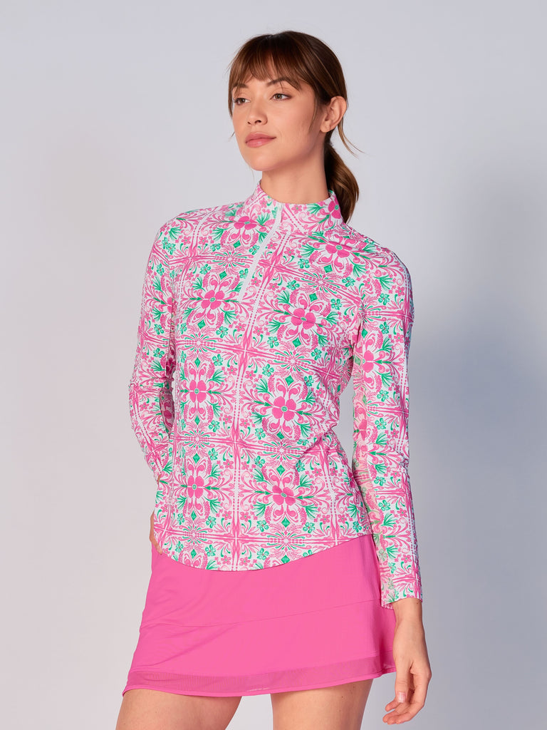 A woman models the G Lifestyle Quarter Zip Sun Protection Top in Pink Tile – symmetrical ornamental print of the Spring Summer 2024 Collection. The top has long sleeves, an adjustable mock neck collar with a flat quarter zip. The fabric appears to have a lightweight, subtle texture, that likely offers menthol cooling, moisture wicking, breathability, sun safety and comfort. Suitable for golf, tennis, padel tennis, pickleball or even cycling.