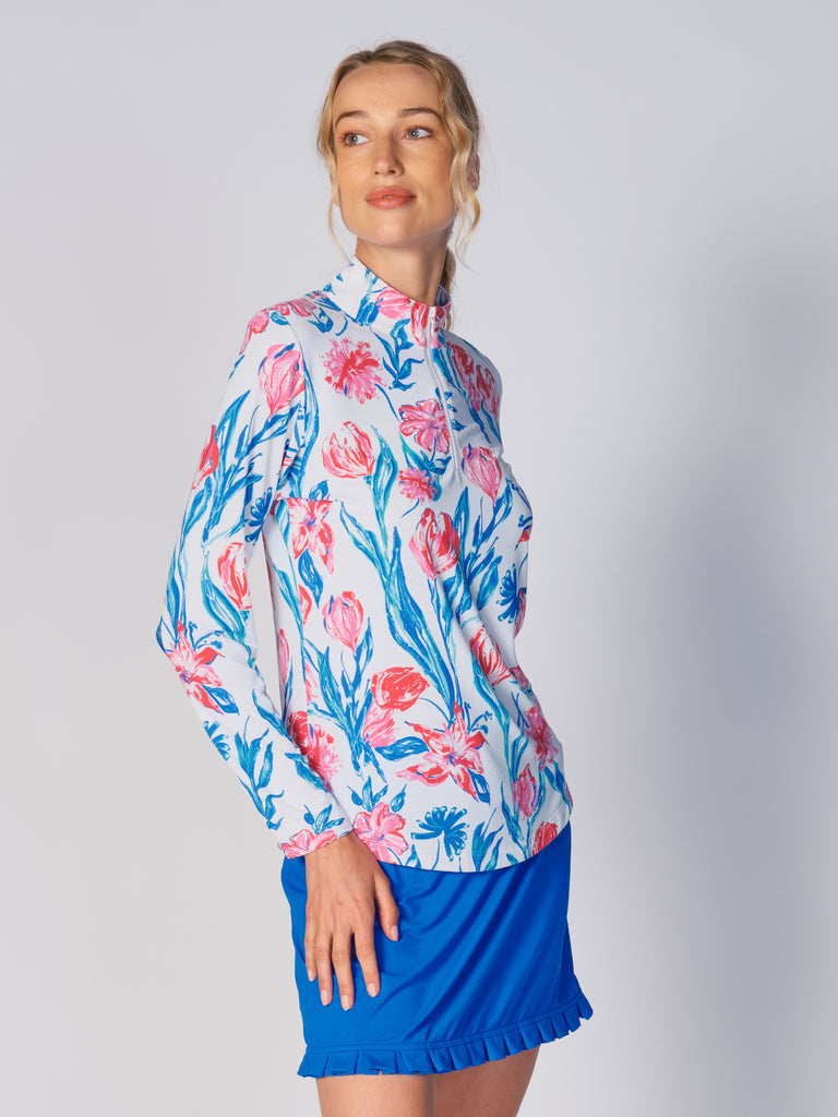 A woman models the G Lifestyle Quarter Zip Sun Protection Top in Tulip - floral print of the Spring Summer 2024 Collection. The top has long sleeves, an adjustable mock neck collar with a flat quarter zip. The fabric appears to have a lightweight, subtle texture, that likely offers menthol cooling, moisture wicking, breathability, sun safety and comfort. Suitable for golf, tennis, padel tennis, pickleball or even cycling.