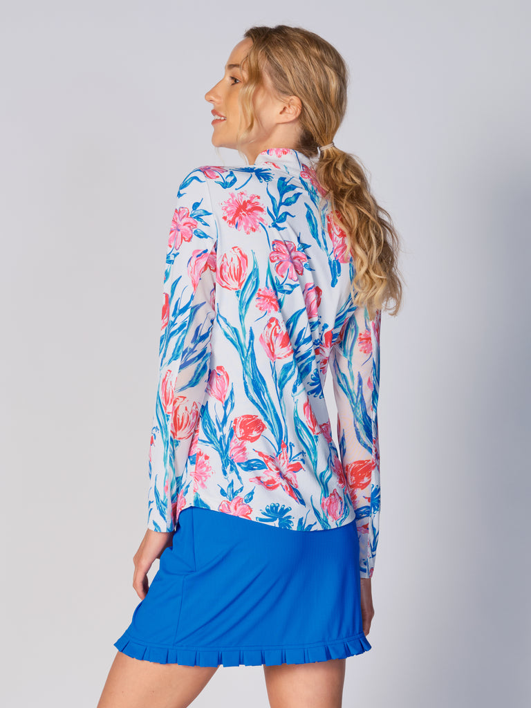 A woman is showcasing the back of the G Lifestyle Quarter Zip Sun Protection Top in Tulip -floral print of the Spring Summer 2024 Collection. The top is tailored with a form-fitting silhouette, complete with long sleeves and a high collar for maximum sun protection. Notably, it includes smooth mesh underarm inserts, which are seamlessly integrated for enhanced breathability, ensuring comfort during active use.