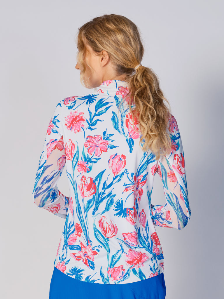 A woman is showcasing the back of the G Lifestyle Quarter Zip Sun Protection Top in Tulip -floral print of the Spring Summer 2024 Collection. The top is tailored with a form-fitting silhouette, complete with long sleeves and a high collar for maximum sun protection. Notably, it includes smooth mesh underarm inserts, which are seamlessly integrated for enhanced breathability, ensuring comfort during active use.
