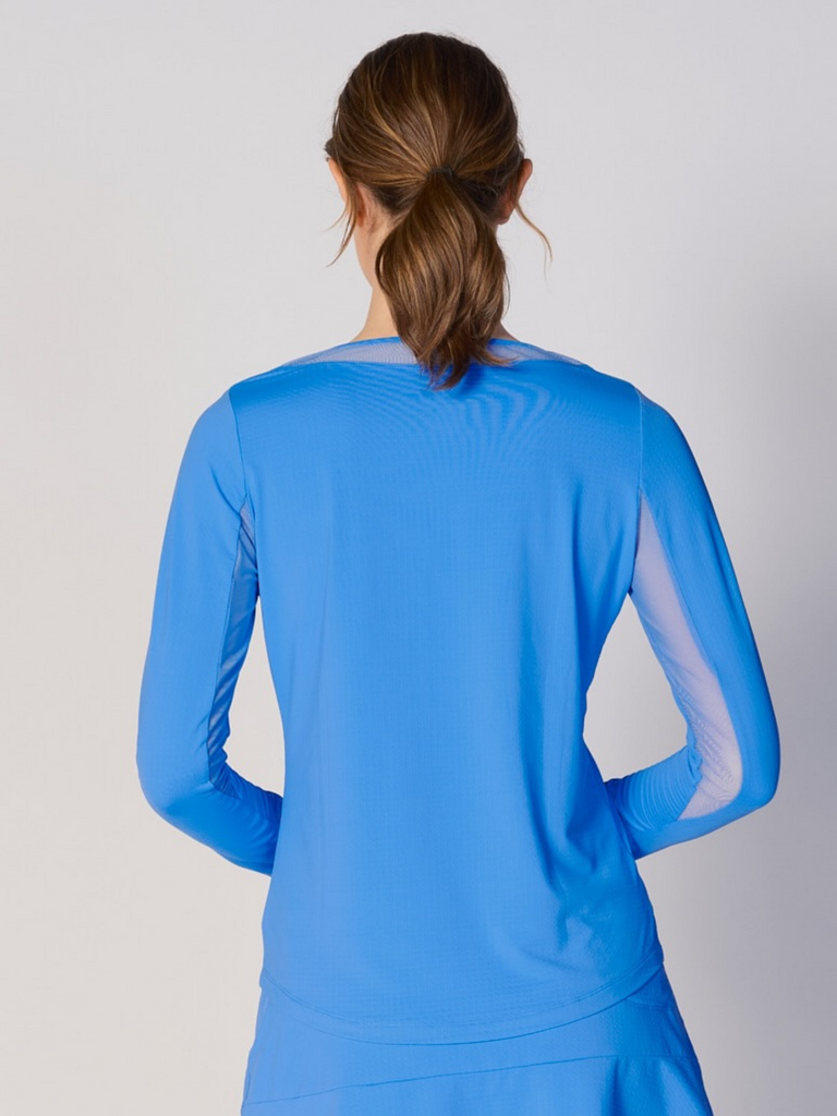 A woman is showcasing the back of the G Lifestyle Mesh Block Long Sleeve Top in Bright Peri. The top is tailored with a snug fit silhouette, complete with long sleeves and round neckline with mesh details. Notably, it includes smooth mesh underarm inserts, which are seamlessly integrated for enhanced breathability, ensuring comfort during active use. 
