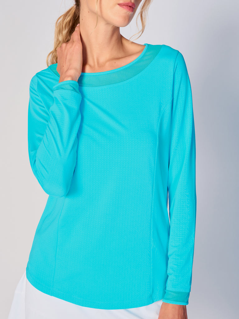A woman wears G Lifestyle Mesh Block Long Sleeve Top in Caribbean Turquoise. The top is designed with long sleeves, mesh underarm inserts for breathability, and features a round neckline with texture mesh block detailing around it and sleeve hems. The fabric appears to be lightweight, movement-friendly, with subtle texture. Suitable for various outdoor athletic activities such as golf, tennis, padel tennis, pickleball or even cycling.