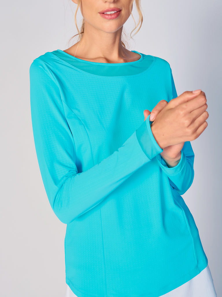 A woman wears G Lifestyle Mesh Block Long Sleeve Top in Caribbean Turquoise. The top is designed with long sleeves, mesh underarm inserts for breathability, and features a round neckline with texture mesh block detailing around it and sleeve hems. The fabric appears to be lightweight, movement-friendly, with subtle texture. Suitable for various outdoor athletic activities such as golf, tennis, padel tennis, pickleball or even cycling.