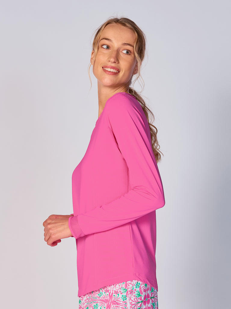 A woman is showcasing the side of the G Lifestyle Mesh Block Long Sleeve Top in Hot Pink. The top is designed with long sleeves, mesh underarm inserts for breathability, and features a round neckline with texture mesh block detailing around it and sleeve hems. The fabric appears to be lightweight, movement-friendly, with subtle texture. Suitable for various outdoor athletic activities such as golf, tennis, padel tennis, pickleball or even cycling.